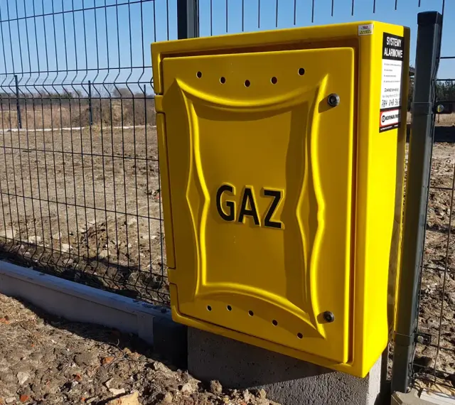 Żółta skrzynka gazowa z napisem "GAZ" przy ogrodzeniu. Zastanawiasz się, ile kosztuje przyłącze gazu?