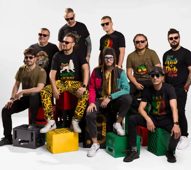 Grupa mężczyzn w koszulkach z motywami nawiązującymi do rastafarianizmu. Jeden z nich ma dredy i kolorową kurtkę, co może kojarzyć się z tym, czym jest rastafarianizm.