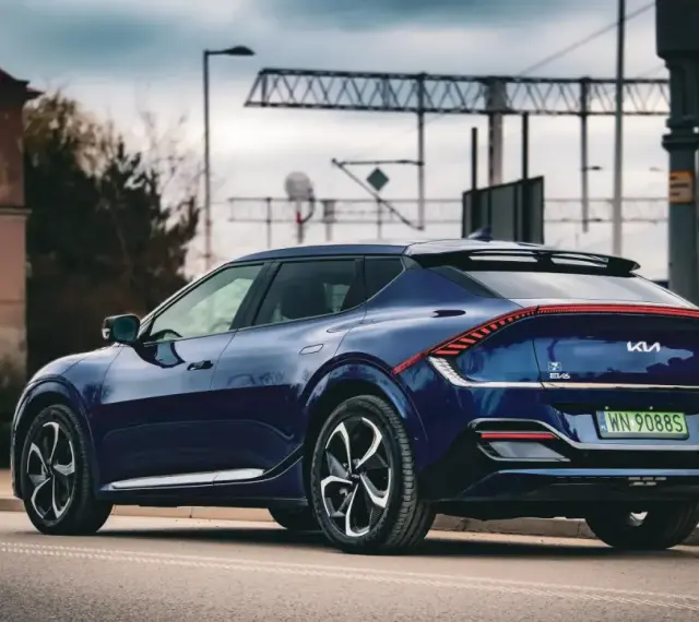 Granatowe Kia EV6 GT z charakterystycznym pasem świateł z tyłu, zaparkowane przy drodze z widoczną infrastrukturą kolejową.