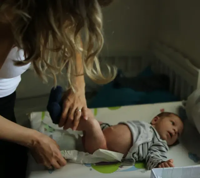 Mama zmienia pieluszkę noworodkowi. Zastanawiasz się, ile kupić pieluszek dla noworodka? Warto mieć zapas!