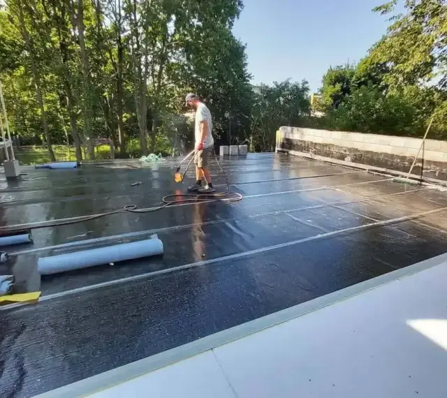 Pracownik wykonuje hydroizolację tarasu nad garażem, używając palnika do zgrzewania papy.