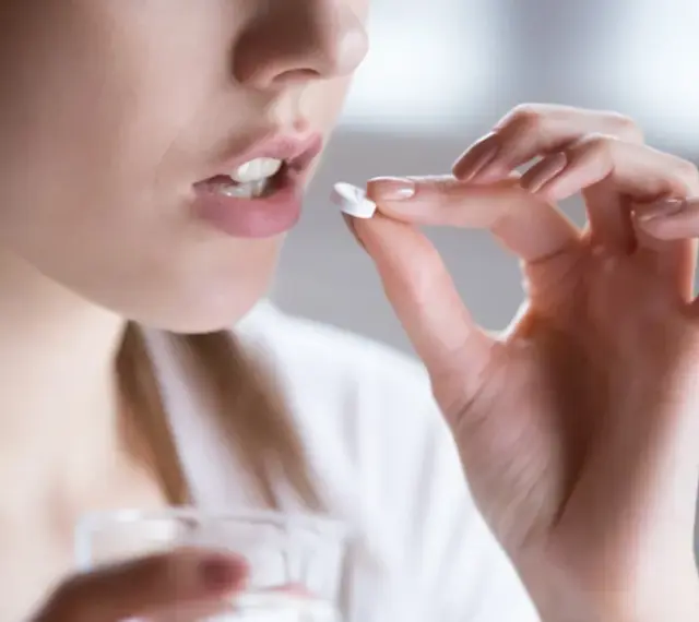 Kobieta bierze tabletkę clindamycin mip 600, trzymając szklankę wody.