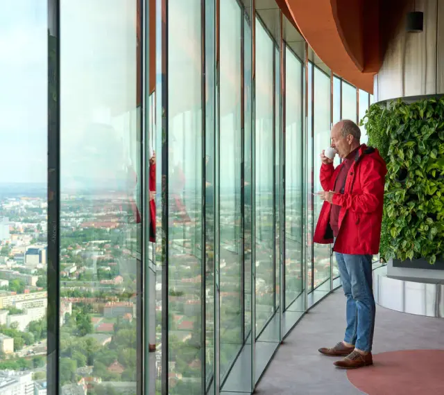 Mężczyzna pije kawę, podziwiając panoramę Wrocławia z tarasu widokowego. Sprawdź sky tower wrocław cennik, by poznać ceny biletów.