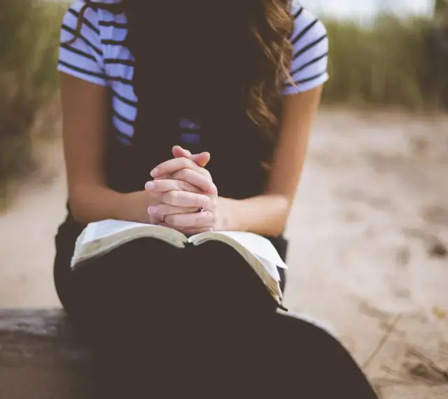 Kobieta z dłońmi złożonymi nad otwartą Biblią. To jej modlitwa o dobry dzień w pracy.
