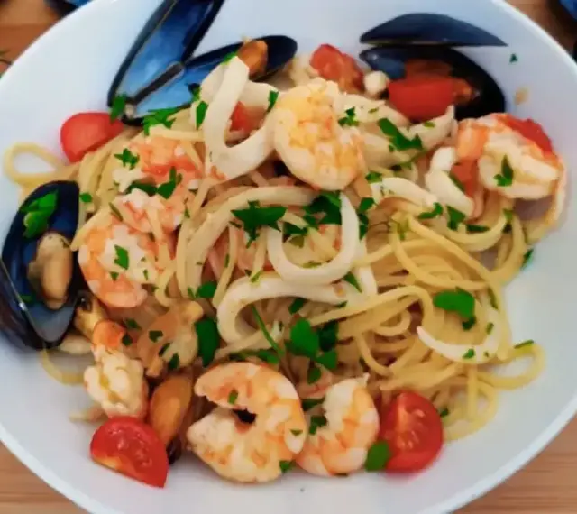 Pyszne linguini z krewetkami, kalmarami i małżami, ozdobione pomidorkami i natką pietruszki.