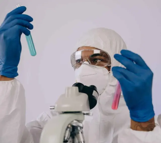Badacz w kombinezonie i masce analizuje próbki w probówkach, przygotowując się do pracy w laboratorium chemicznym.