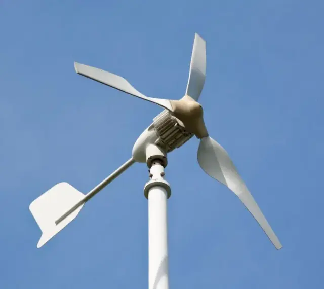 Biała elektrownia wiatrowa z trzema łopatami na tle błękitnego nieba.