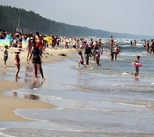 Ludzie kąpią się w Bałtyku, szukając miejsca, gdzie jest najcieplejsza woda. Słoneczny dzień na plaży z rodzinami i dziećmi.
