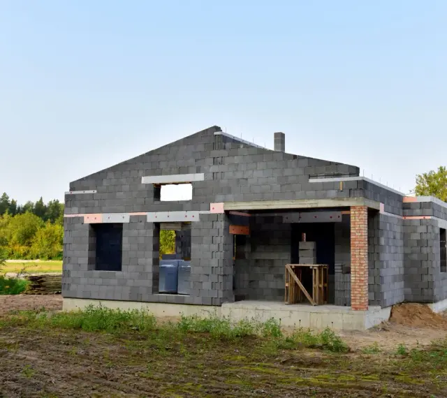Budowa domu z keramzytu. Widać niedokończone ściany z bloczków, otwory okienne i drzwiowe. Brak dachu i wykończenia.