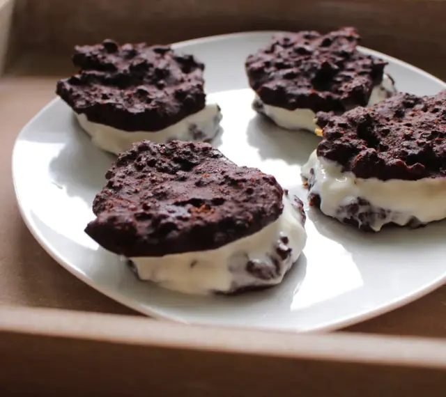 Cztery domowe ciastka z kremem, przypominające Oreo, na białym talerzu. Pyszna przekąska, choć warto sprawdzić oreo kcal przed zjedzeniem.
