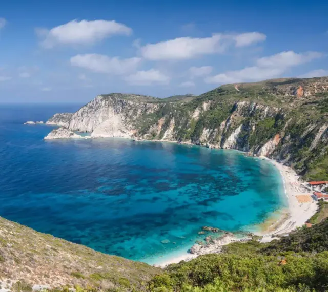 Malownicza zatoka z turkusową wodą i piaszczystą plażą, otoczona stromymi, zielonymi klifami. To idealne miejsce na wypoczynek na wyspie na Morzu Jońskim.