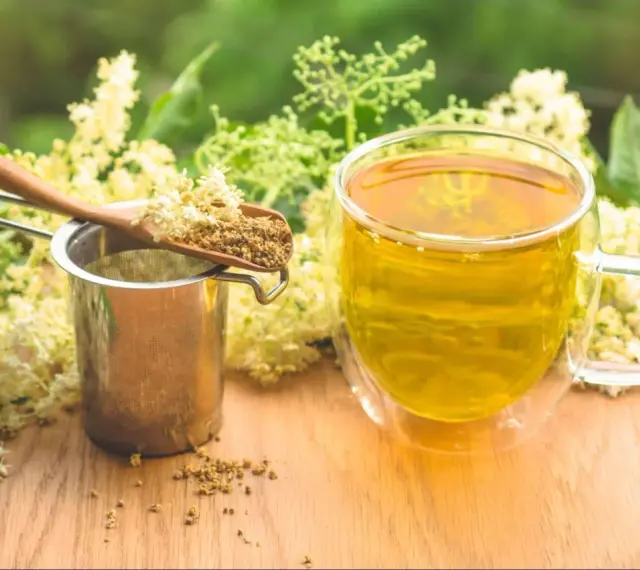 Aromaticzny napar z czarnego bzu, suszone kwiaty na łyżce i metalowe sitko.