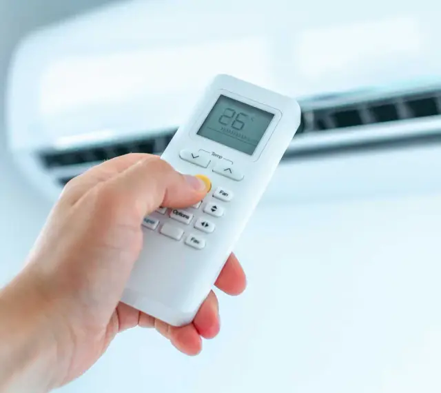 Dłoń trzymająca pilot do klimatyzatora, ustawiająca temperaturę. Ogrzewanie klimatyzatorem to komfort.