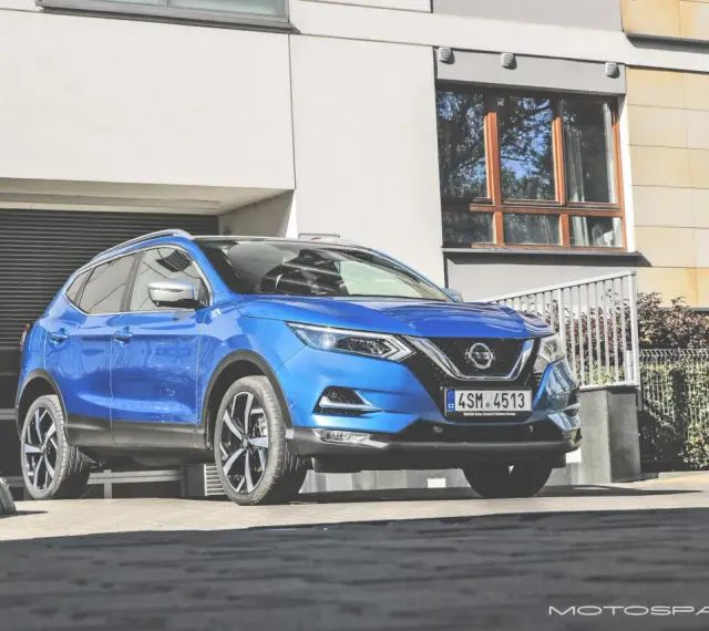 Błękitny Nissan Qashqai 2018 zaparkowany przed nowoczesnym budynkiem z garażem.