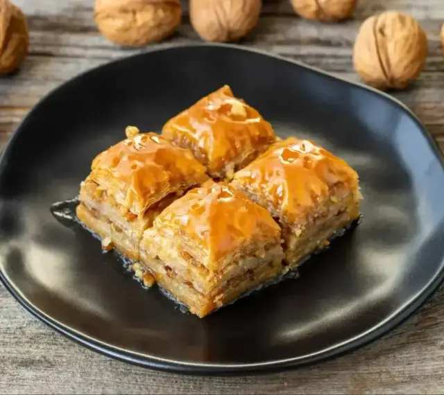 Słodka baklawa na czarnym talerzu, idealna do domowego przepisu. Orzechy włoskie w tle.