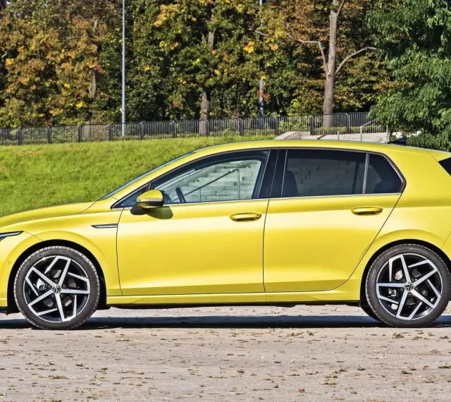 Żółty hatchback Volkswagen Golf VIII z przyciemnianymi szybami stoi na tle zieleni i drzew.