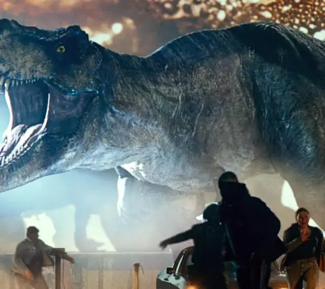 Gigantyczny Tyranozaur Rex z Jurassic World 3 z otwartą paszczą ściga ludzi wśród samochodów.