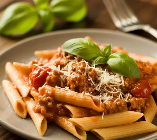 Penne z sosem bolognese, posypane parmezanem i udekorowane bazylią. Pyszne potrawy włoskie na talerzu.