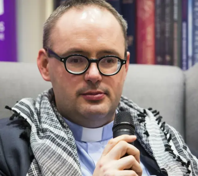 Ksiądz Kaczkowski, w okularach i z szalem, dzieli się cytatami o życiu.