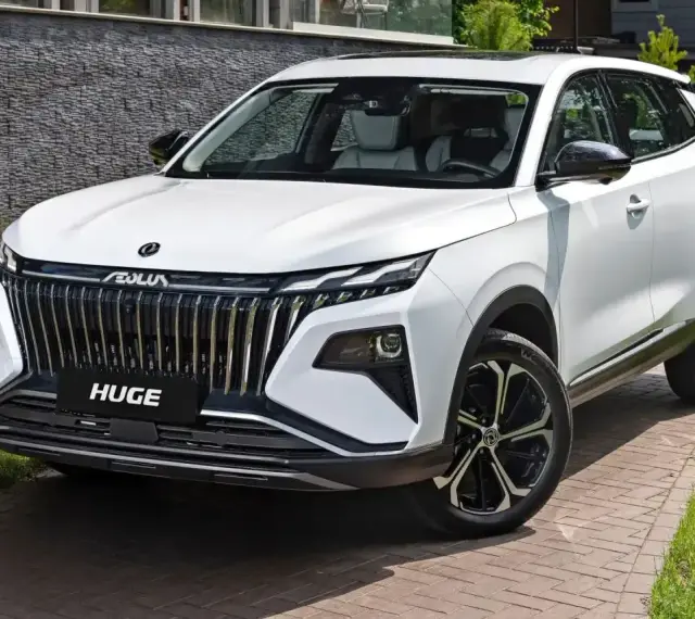 Nowy, biały chinski suv z imponującym grillem i felgami stoi na podjeździe.