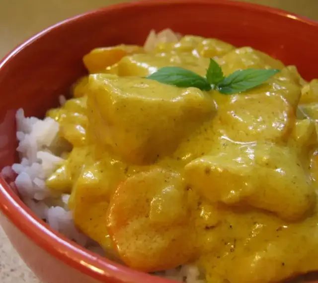 Miseczka ryżu z kurczakiem w kremowym sosie z curry, ozdobiona listkiem mięty.