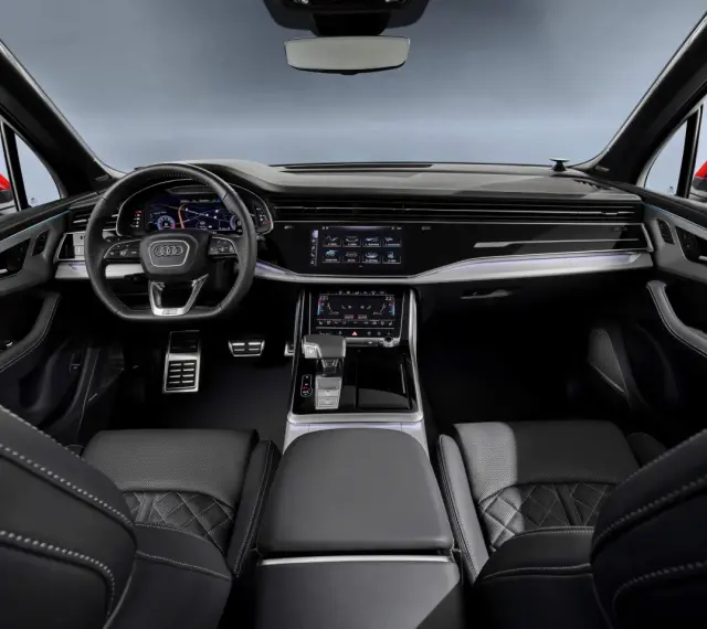 Wnętrze Audi Q7 z ekranami, kierownicą i skórzanymi fotelami.