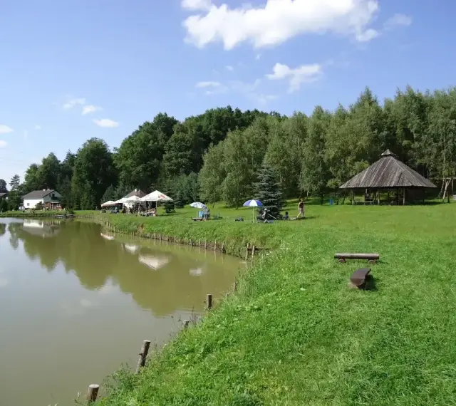 Malownicze dzikie łowiska Małopolska: spokojna woda, zielone wzgórza, drewniana altana i miejsca do wypoczynku.