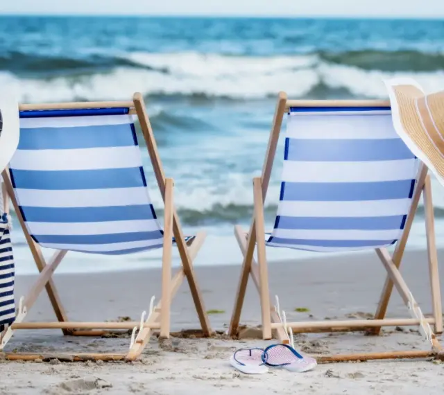Dwa leżaki na plaży, gotowe na idealny weekend nad morzem. W tle fale, a obok kapelusze i torba plażowa.
