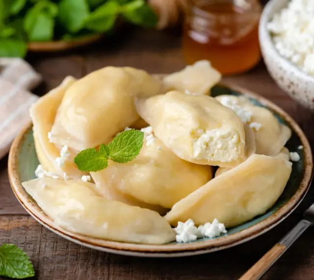 Pyszne pierogi z serem, jak u babci. Delikatne ciasto i kremowe nadzienie, posypane świeżym twarogiem i miętą.
