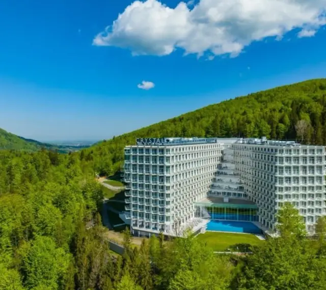 Nowoczesny Crystal Mountain Hotel Wisła otoczony zielonymi wzgórzami, z basenem i tarasami.