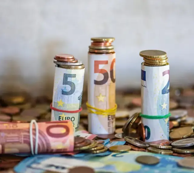Zwijane banknoty euro i monety, symbolizujące kwotę darowizny wolną od podatku, tworzą stosy na tle innych monet.