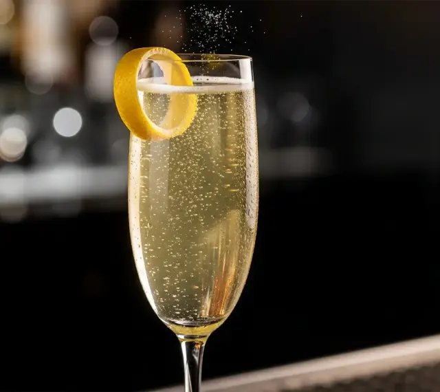 Ett glas French 75 med bubblor och citronskal. En klassisk drink med en intressant french 75 historia.