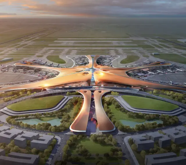 Futurystyczny terminal lotniska, przypominający rozgwiazdę, z samolotami na płycie. To największe lotnisko na świecie, z nowoczesną architekturą i otaczającą zielenią.