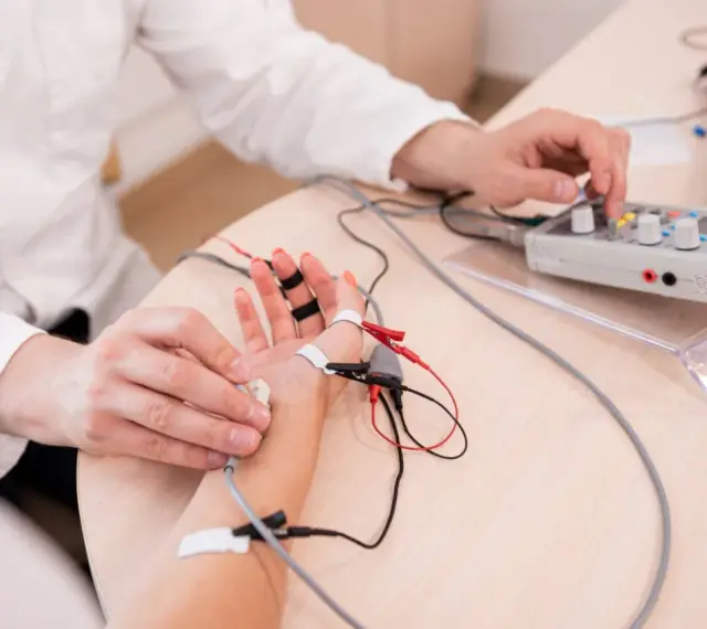 Lekarz wykonuje próbę tężyczkową, podłączając elektrody do dłoni pacjenta i regulując aparat.