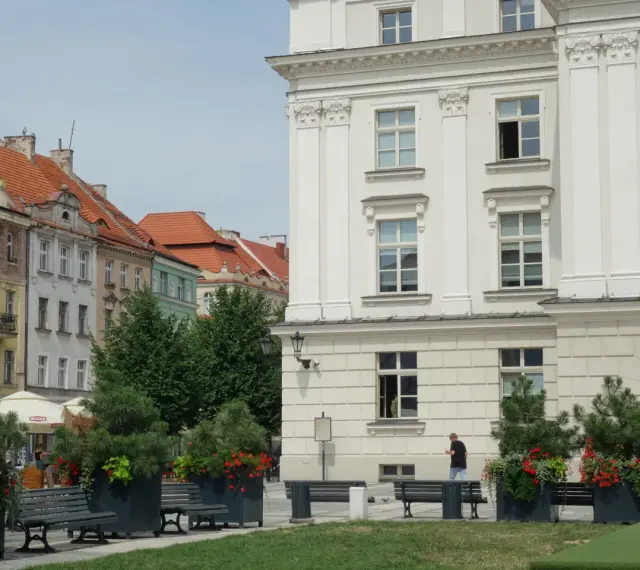 Urokliwe miasto nad Prosną z zabytkową architekturą, zielenią i ławkami w centrum.