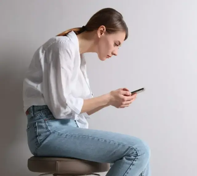 Frau mit gebeugtem Rücken und Handy. Schlechte Haltung kann zu einem Buckel im Nacken Ursache sein.