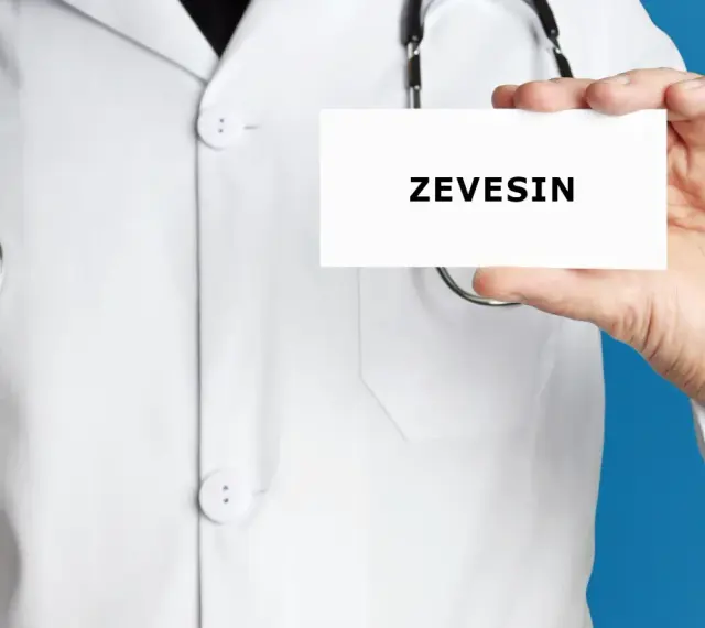 Lekarz w białym kitlu trzyma kartkę z napisem ZEVEISIN. Stetoskop wisi na jego szyi.
