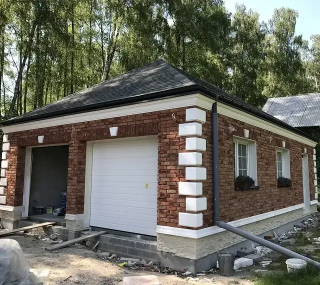 Nowy garaż z cegły z białym gzymsem i ozdobnymi elementami.
