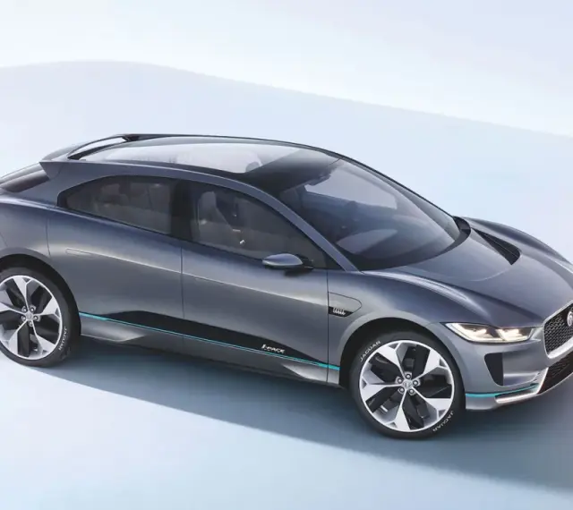Elegancki, szary Jaguar I-PACE, niczym czarny jaguar gotowy do skoku, prezentuje swoją aerodynamiczną sylwetkę na jasnym tle.
