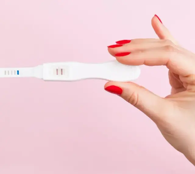 Dłoń z czerwonymi paznokciami trzyma test ciążowy z dwoma kreskami. To może być sygnał, że doszło do ciąży biochemicznej.