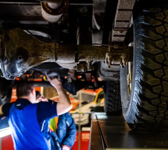 Mechanik bada podwozie terenowego Forda 4x4. Widoczna masywna oś i bieżnik opony.