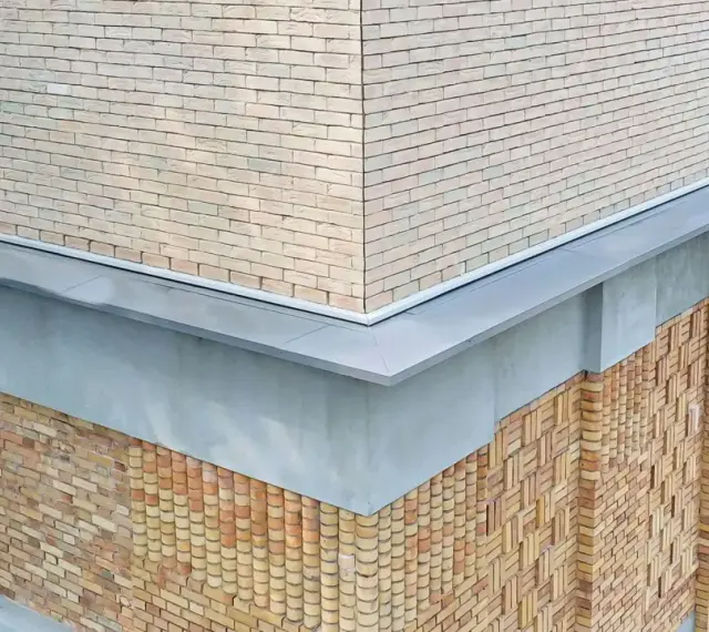 Narożnik budynku z ceglaną elewacją i nowoczesną attyką. Detale architektoniczne podkreślają fakturę muru.