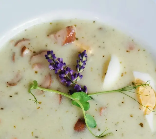 Aromaticzny żurek z kiełbasą i jajkiem, ozdobiony gałązką lawendy i kiełkami.