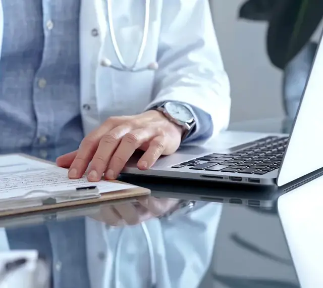 Lekarz w białym kitlu pisze na dokumentach, obok laptop. Zastanawia się, ile można być na zwolnieniu lekarskim od psychiatry.