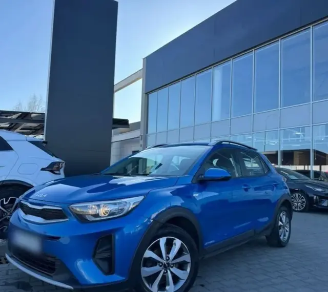 Błękitny Kia Stonic 2023 zaparkowany przed salonem samochodowym. Obok stoi biały SUV.