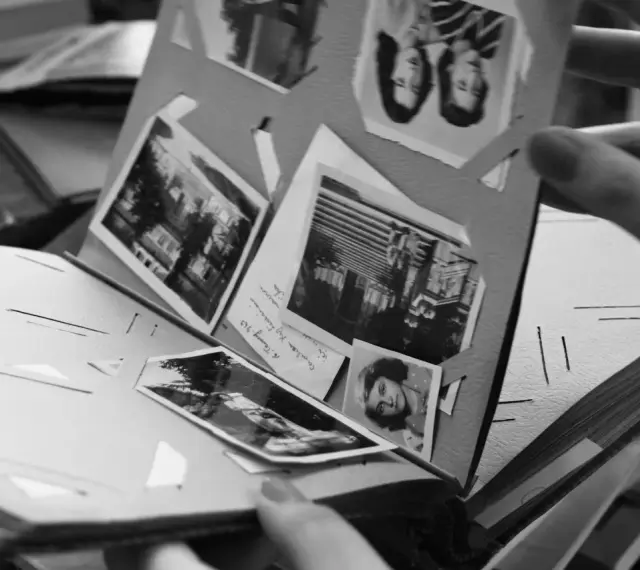 Odkryj, jak zrobić fotoksiążkę, przeglądając stare zdjęcia w albumie. Ręka trzyma kartę z portretami i krajobrazami.