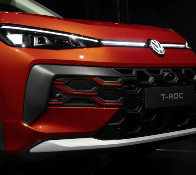 Nowy VW T-Roc w kolorze pomarańczowym prezentuje się z przodu z charakterystycznym grillem i nowoczesnymi światłami IQ.LIGHT.