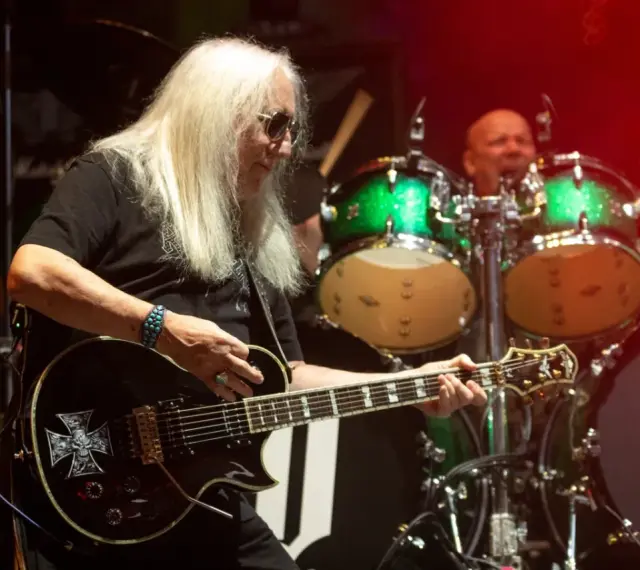 Uriah Heep członkowie na scenie. Mick Box gra na gitarze, a za nim perkusista.