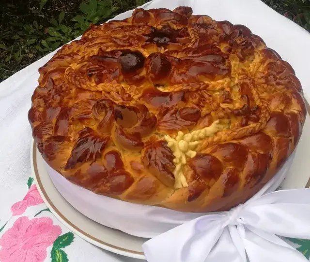 Obrzędowe ciasto weselne, bogato zdobione, z plecionkami i kwiatami z ciasta, na haftowanym obrusie.
