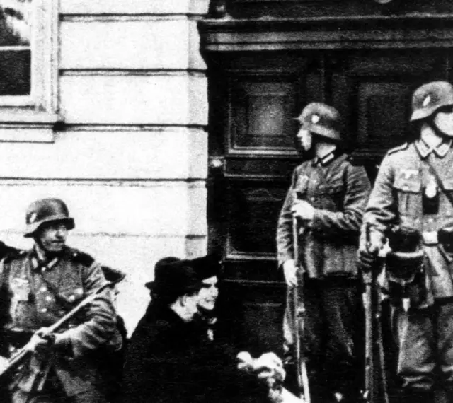 Soldaten der Gestapo stehen Wache. Ein Mann mit Gewehr im Vordergrund, zwei weitere im Hintergrund.